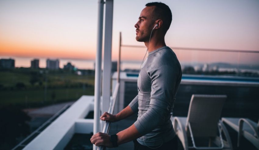 A man is standing on a balcony overlooking the city at sunset.