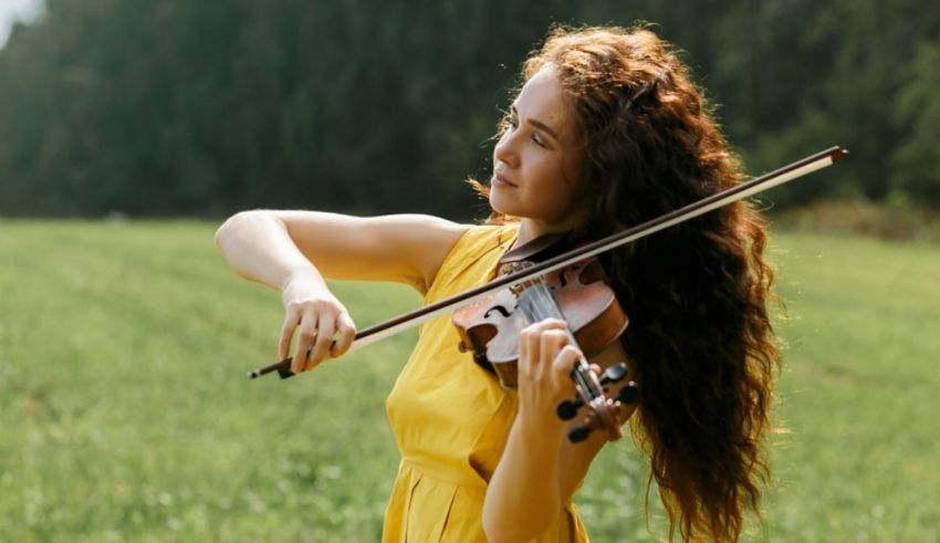 A young woman playing the violin in a field.