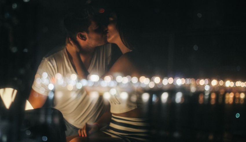 A couple kissing in front of a window at night.