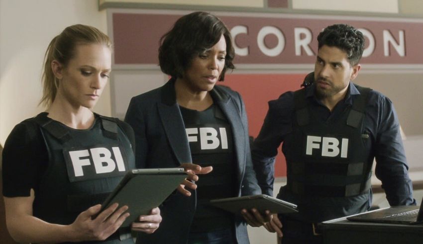 Three people in fbi uniforms looking at a tablet.