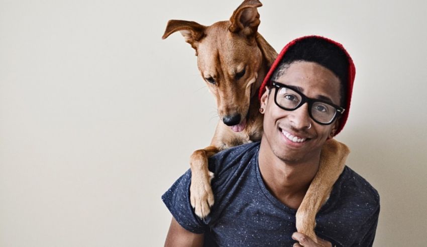 A young man with glasses and a dog on his shoulder.