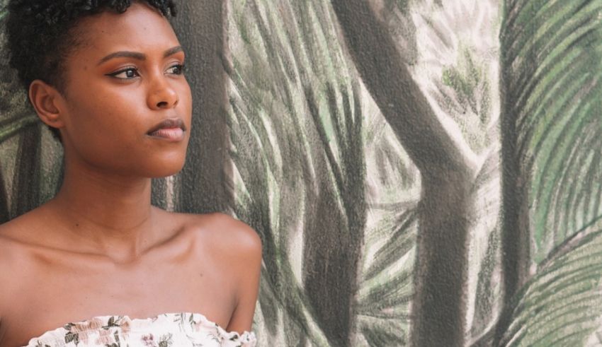 A young african woman in a white dress leaning against a wall.