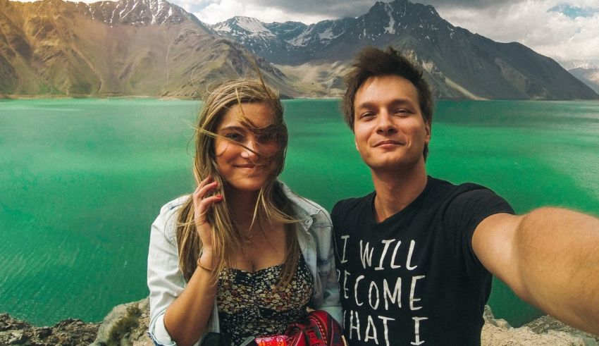 A man and woman taking a selfie in front of a lake.