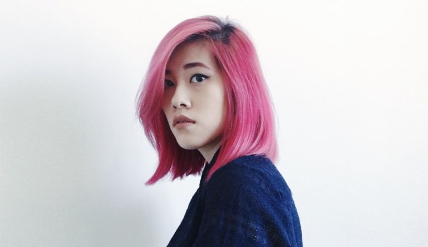 A woman with pink hair posing in front of a white wall.