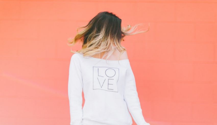 A woman wearing a white off the shoulder sweater with love written on it.