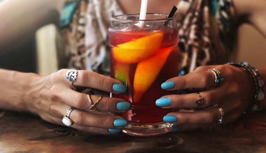 A woman holding a drink with blue nails.