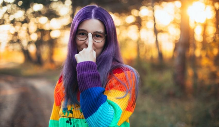 A girl with purple hair is holding her nose in the woods.
