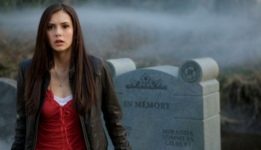 A woman in a red jacket standing next to a gravestone.