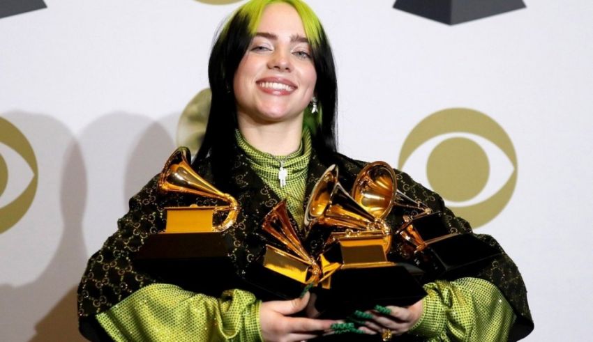 A woman with green hair holding two grammy awards.