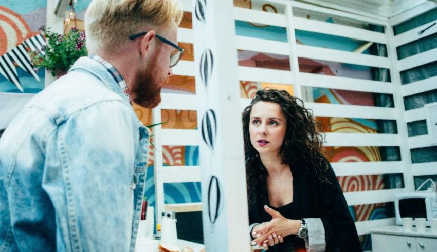 A woman talking to a man in front of a colorful wall.