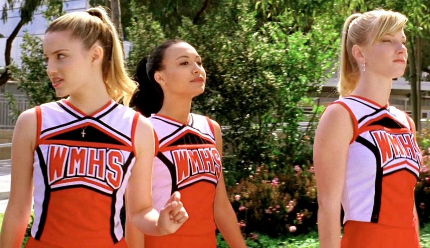 Three cheerleaders in red and orange uniforms standing together.