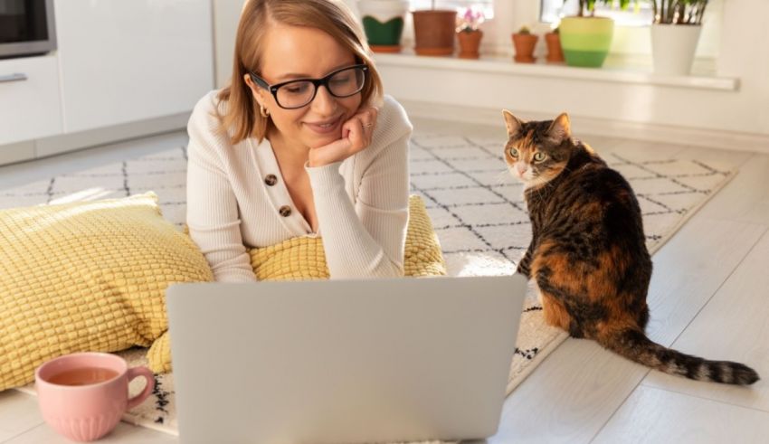 A woman sitting on the floor with a cat and a laptop.