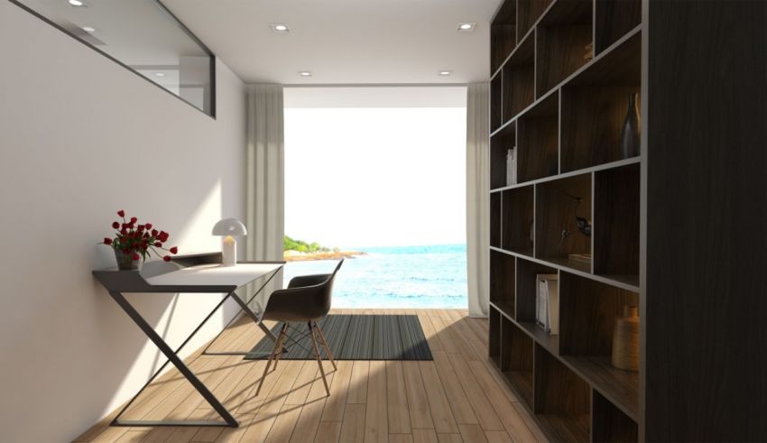 A room with a desk and bookshelves and a view of the ocean.