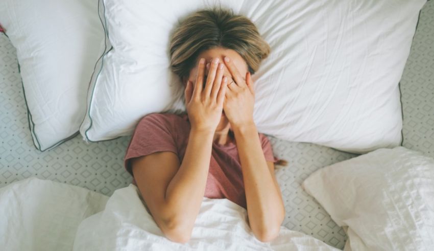 A woman in bed covering her face with her hands.