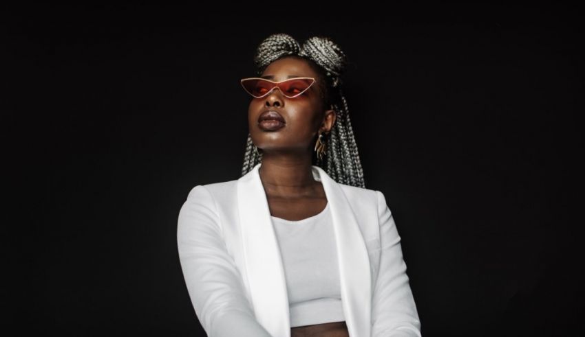 A woman in a white blazer and glasses posing against a black background.