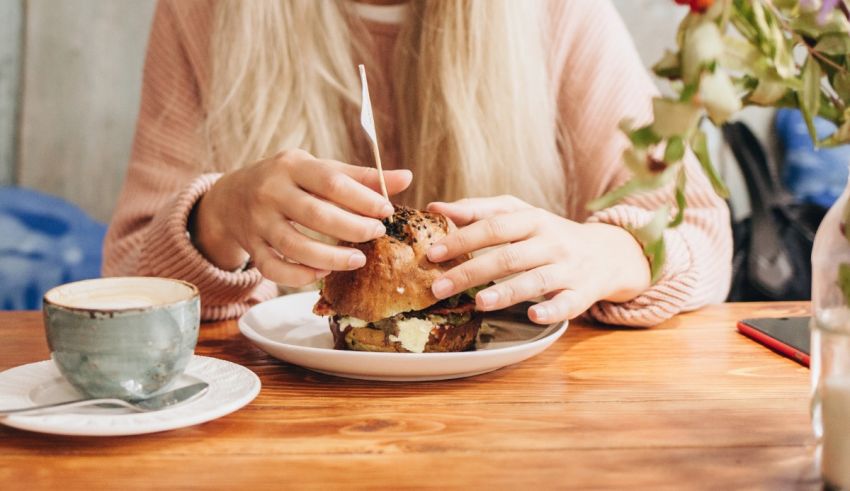 A woman eating a sandwich at a table with a cup of coffee.