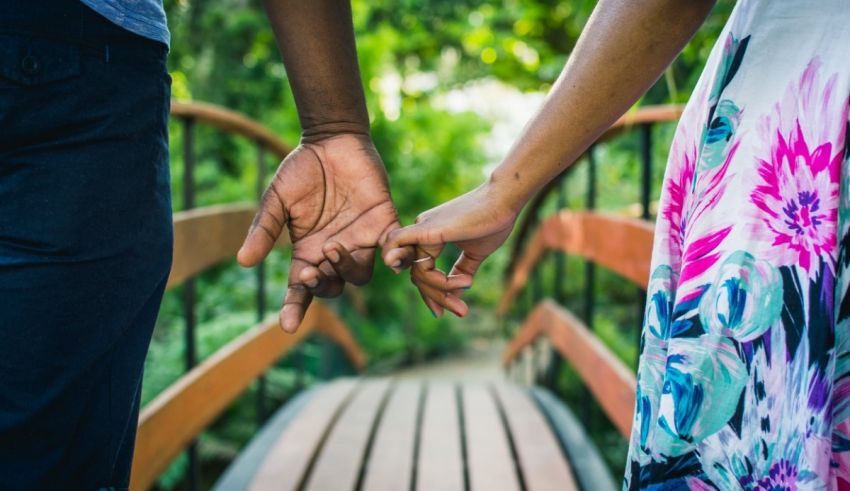 A couple holding hands on a bridge in a garden.