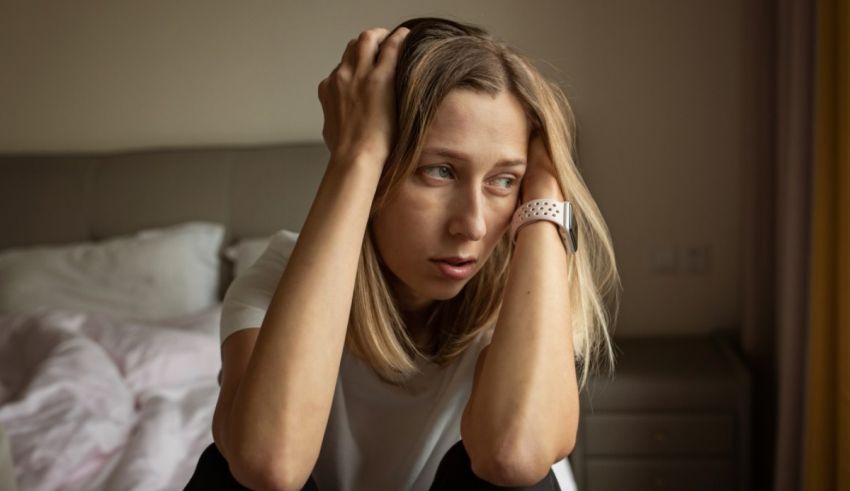 A woman is sitting on a bed with her hands on her head.