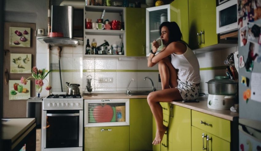 A woman sitting on the edge of a green kitchen.