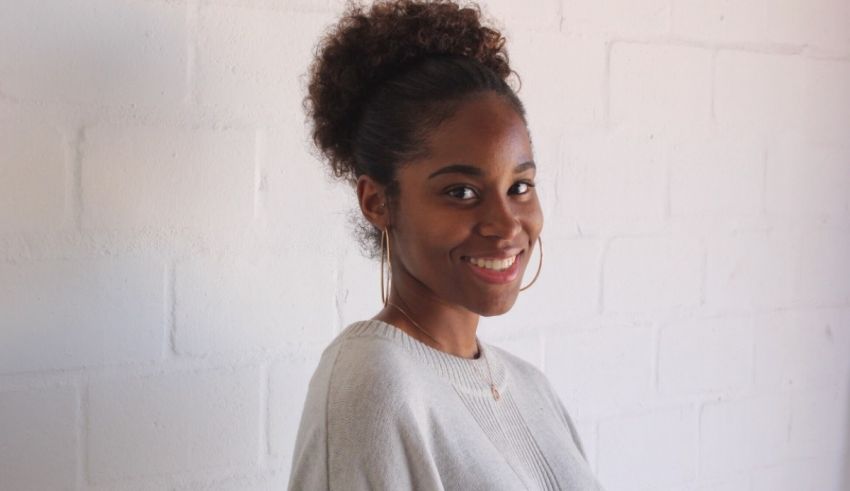 A young black woman smiling in front of a white wall.