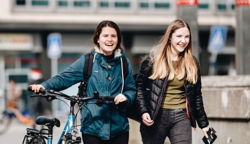 Two young women walking with their bicycles in a city.