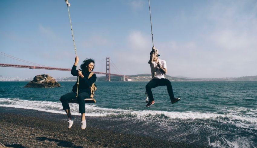 Two people swinging on a rope near the golden gate bridge.