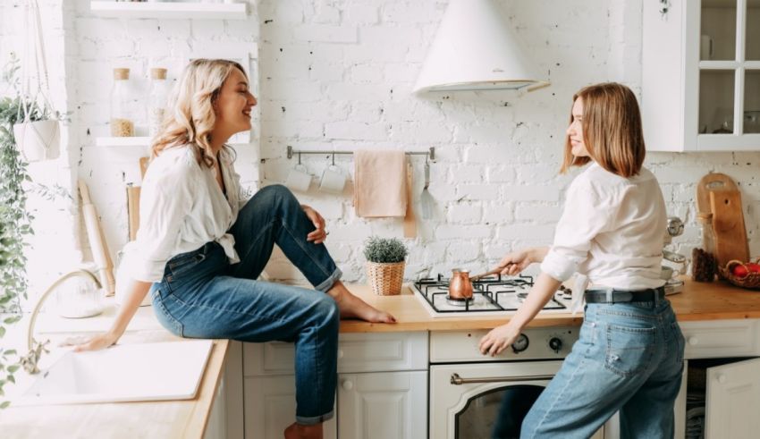 Two women in jeans sitting on a kitchen counter.