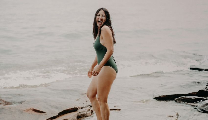A woman in a green swimsuit standing on rocks.