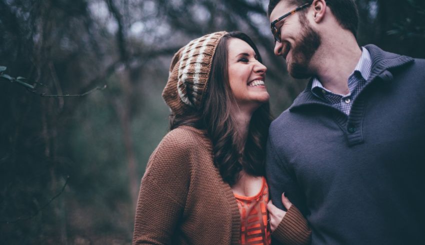 A couple smiles as they walk through the woods.