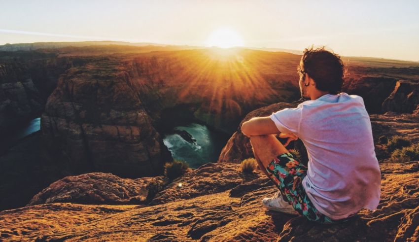 A man sitting on a cliff overlooking a canyon at sunset.