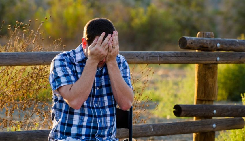 A man in a wheelchair is covering his face with his hands.