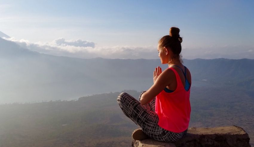 A woman sits on top of a mountain and meditates.