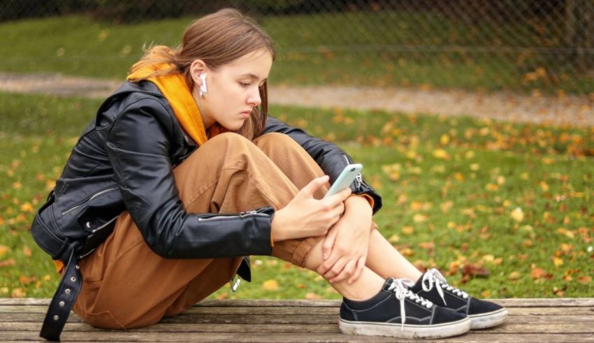 A girl sitting on a wooden bench with a cell phone.