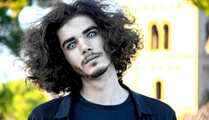 A man with curly hair is standing in front of a building.