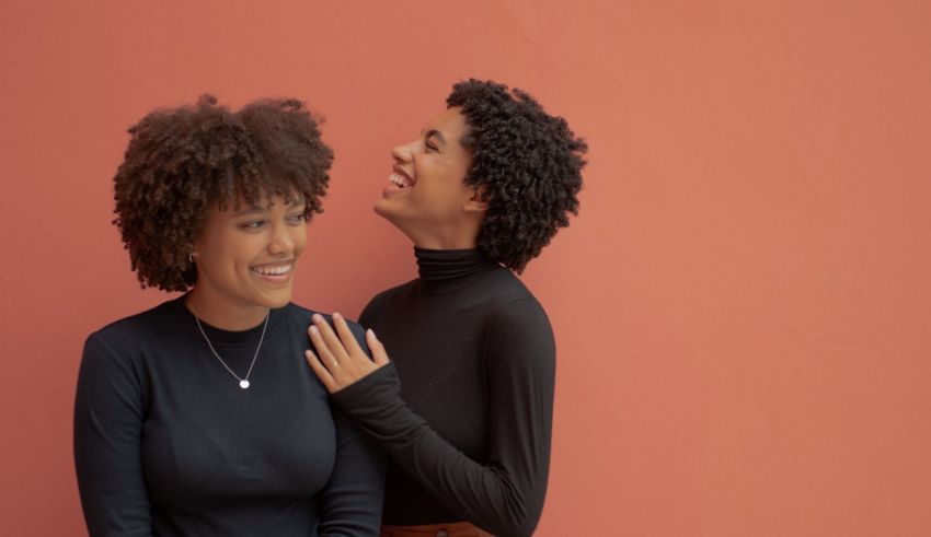 Two afro-american women laughing against an orange wall.