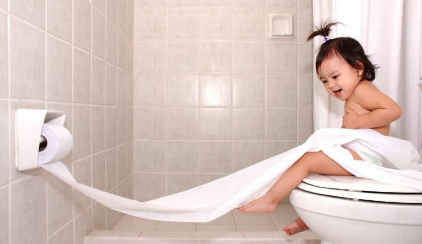 A baby sitting on top of a toilet with a roll of toilet paper.