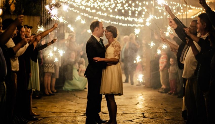 A bride and groom kiss in front of sparklers.