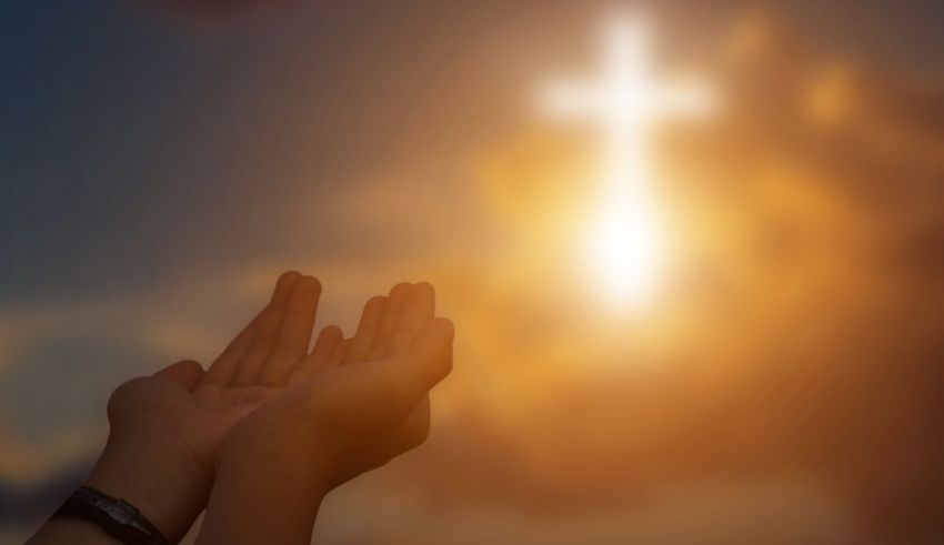 A person's hands reaching up to a cross in the sky.