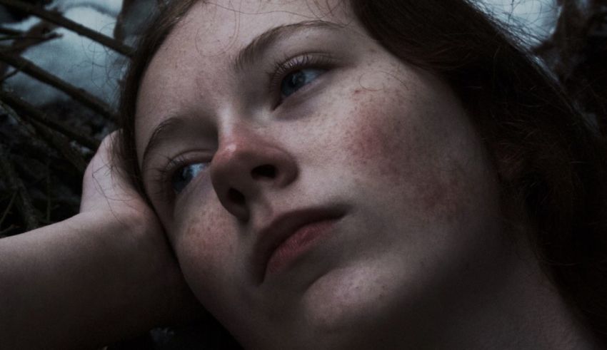 A young girl with freckles laying down in the woods.