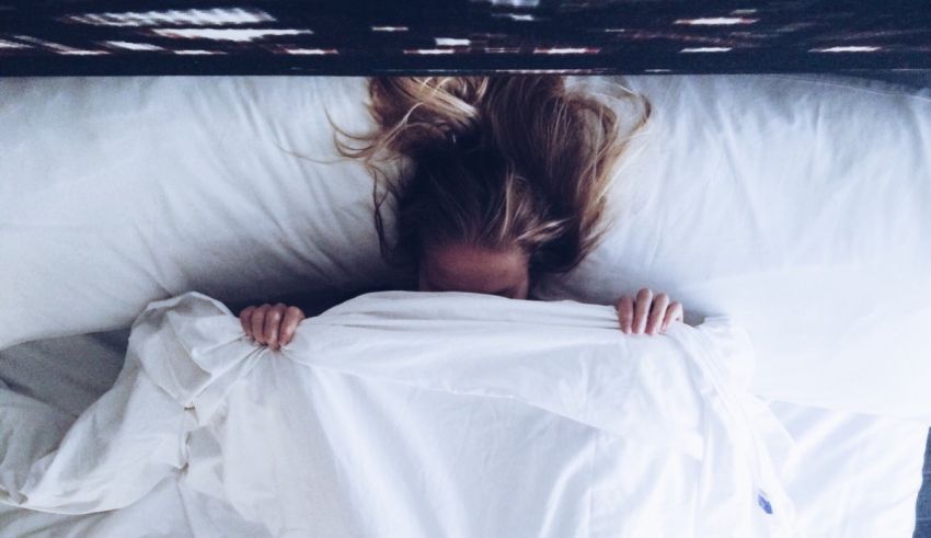 A woman laying in bed with a white blanket over her head.