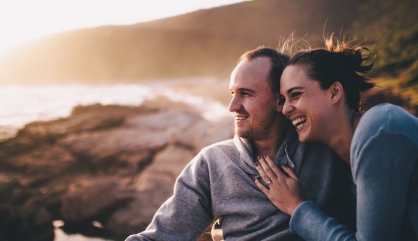 A man and woman are sitting on a rock overlooking the ocean.