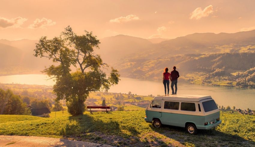 Two people standing on top of a vw camper van overlooking a lake.