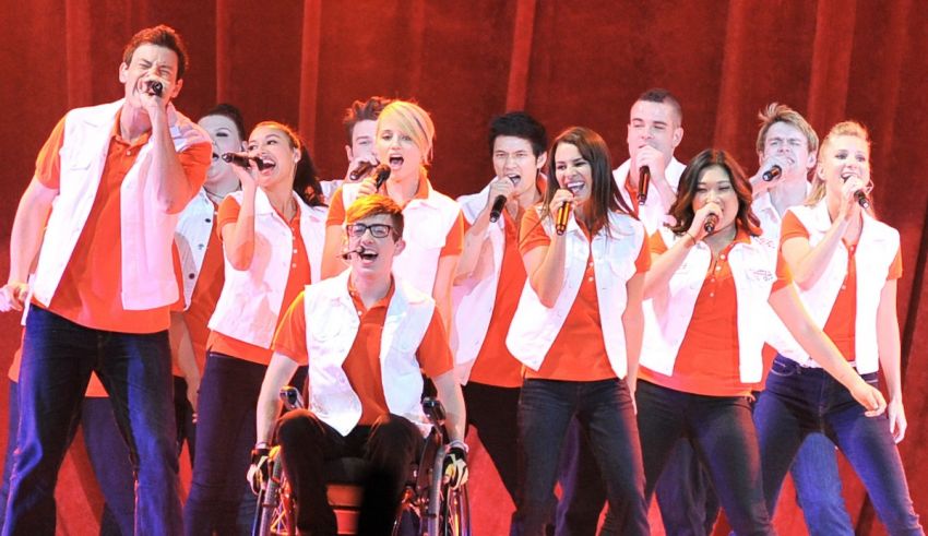 A group of people in orange shirts singing on stage.