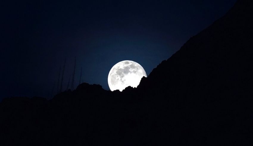 A full moon rising over a mountain.