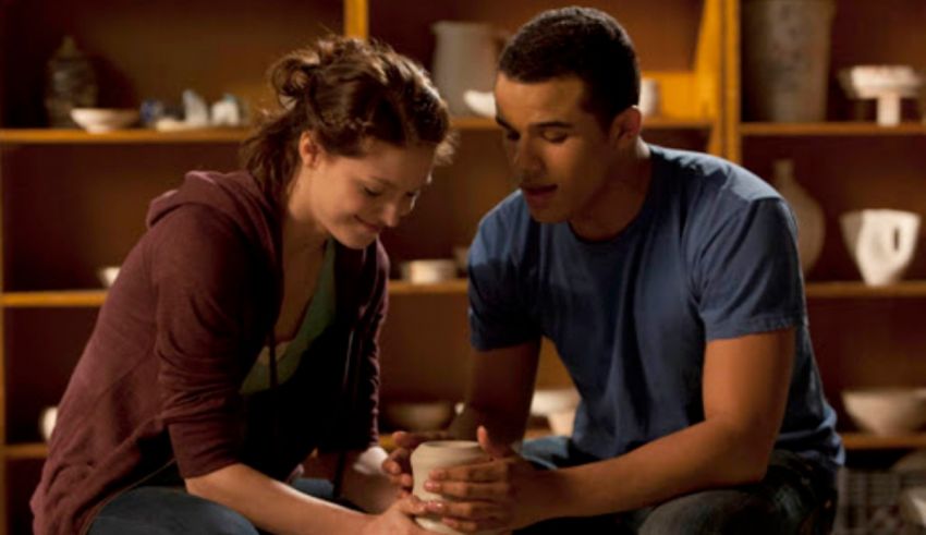 A man and a woman sitting on a floor looking at a cup.