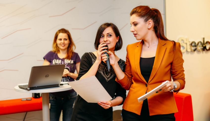 Two women standing in front of a microphone in an office.