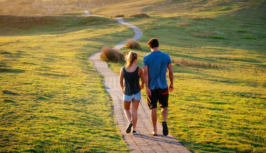 A couple walking down a path in a grassy field.