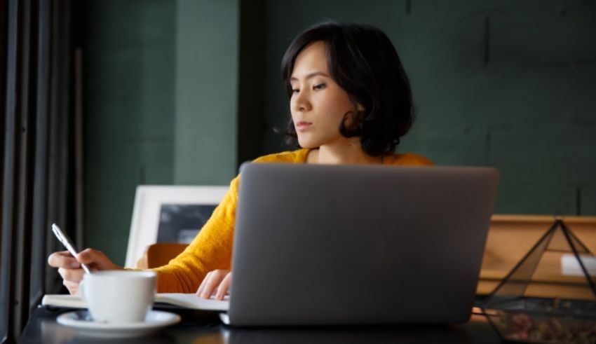 A woman is sitting at a table with a laptop and a cup of coffee.