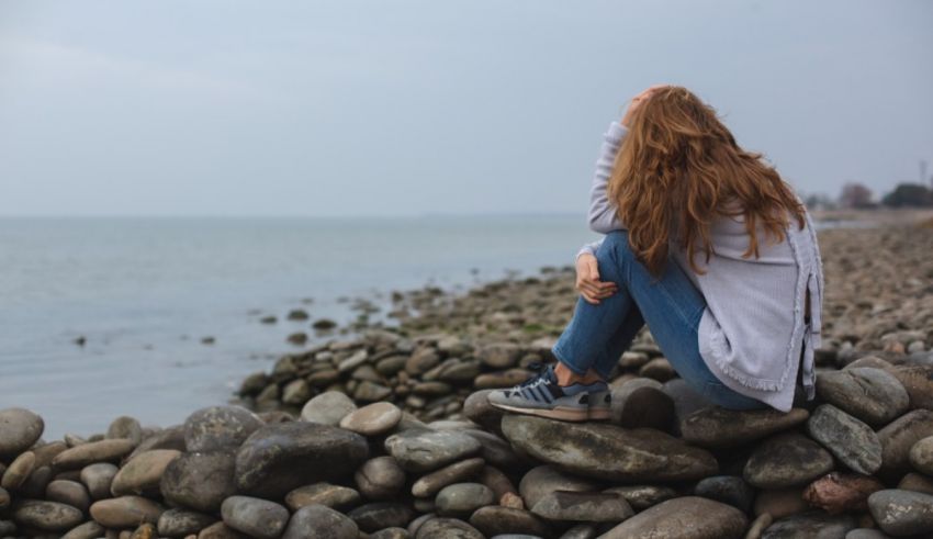 A girl sitting on rocks near the ocean.