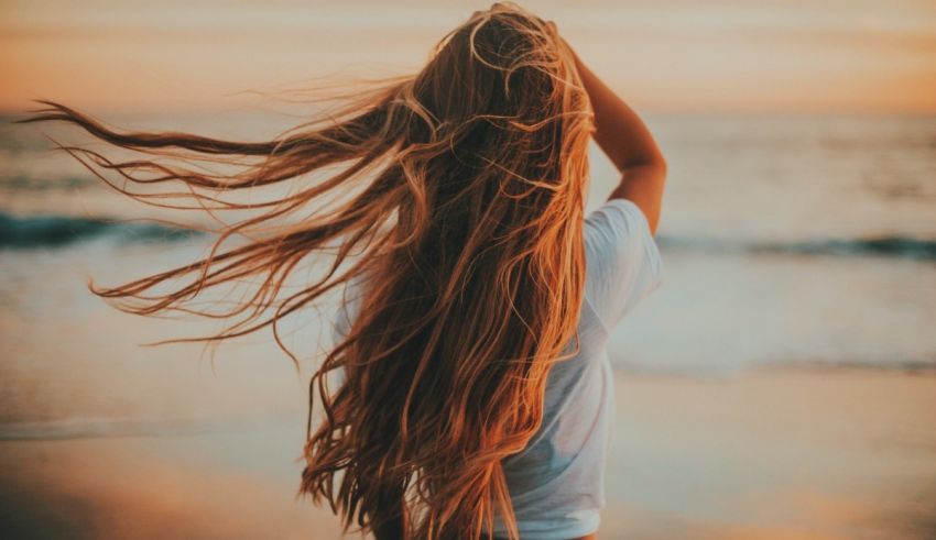 A woman with long hair standing on the beach at sunset.